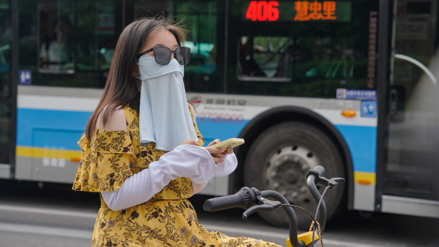 A woman wearing a sunscreen mask uses her cellphone on a street during hot weather in Beijing, China 01 08 2024
